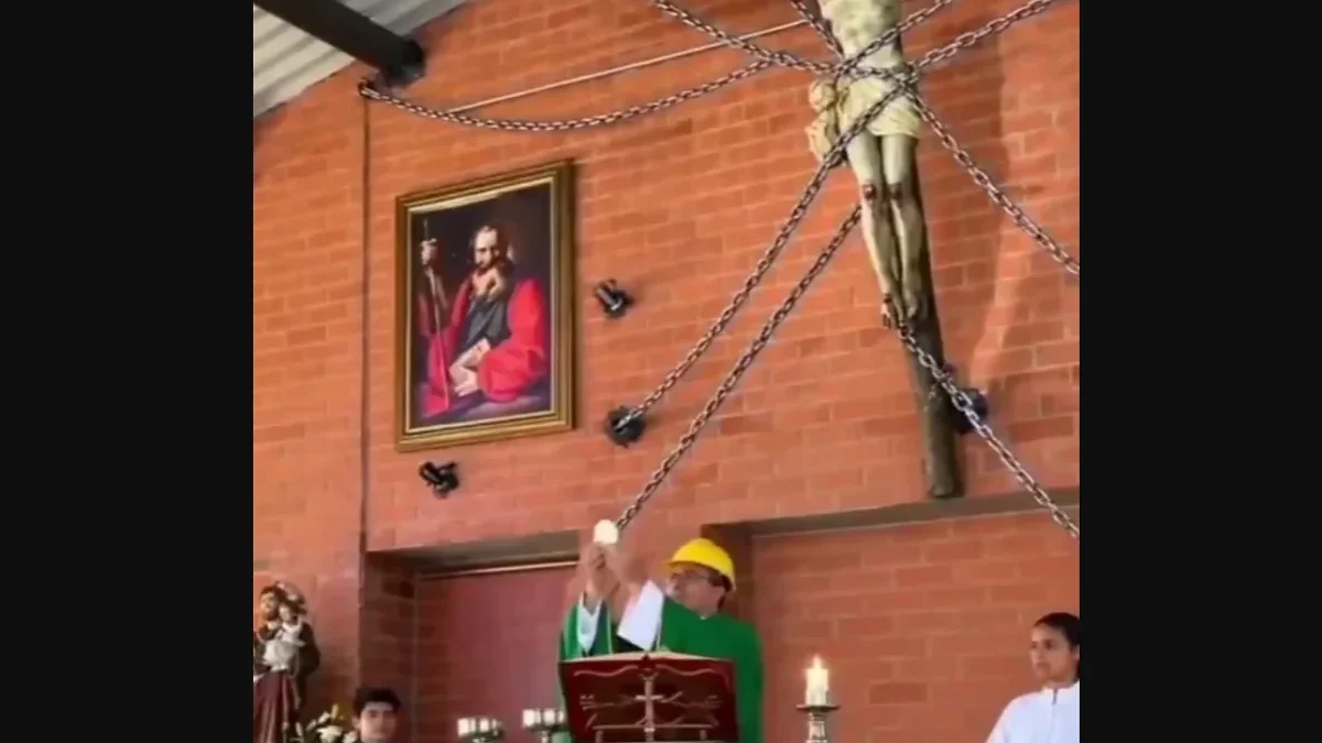 Sacerdote celebra misa con casco frente a una imagen de Cristo asegurada con cadenas