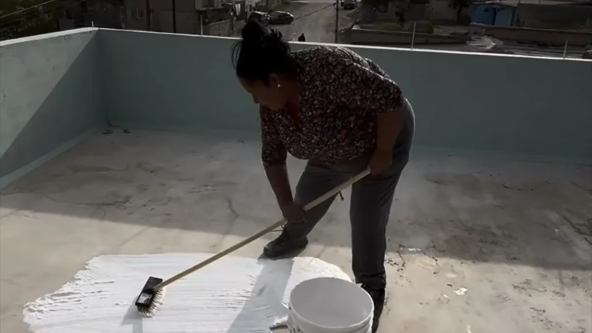 Pache Pache aplica impermeabilizante blanco con un cepillo sobre una azotea en Ciudad Juárez