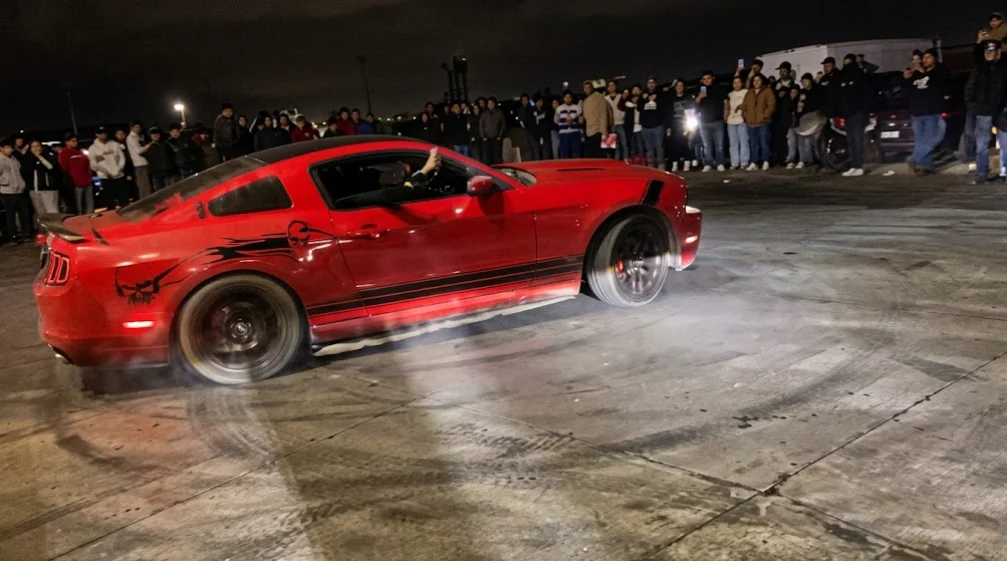 Mustang rojo derrapando frente a una multitud en la Puerta de Juárez