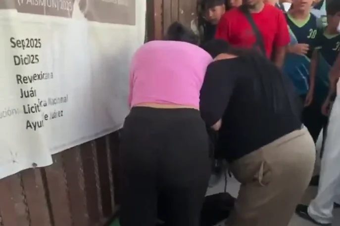 Mujer con blusa rosa inclinada junto a una persona mientras varios jóvenes observan